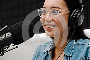 Beautiful happy young woman radio host using microphone and headphones while broadcasting in studio