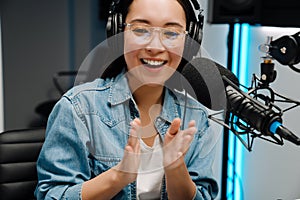 Happy young female radio host using microphone and headphones while broadcasting in studio