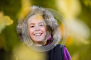 A beautiful happy young girl in a fur lined hood and surrounded by falling leaves