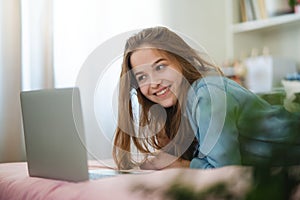 Beautiful happy young girl with laptop lying on bed smiling, online dating concept.