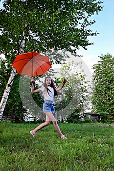beautiful happy young girl with an orange umbrella is having fun on sunny summer day outdoors against the background of green