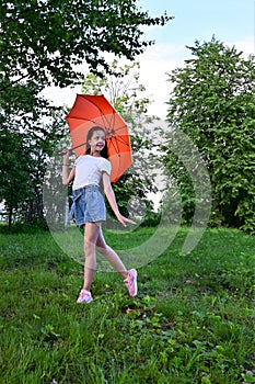 beautiful happy young girl with an orange umbrella is having fun on sunny summer day outdoors in park, dressed in white T-shirt