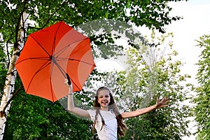 beautiful happy young girl in white T-shirt holds an orange umbrella, having fun on sunny summer day in park against the