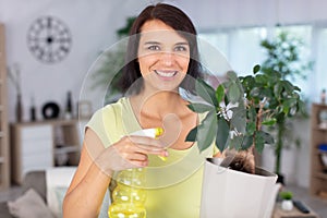 beautiful happy young housewife watering flowers at home