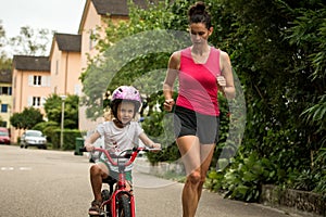 Beautiful and happy young mother teaching her cute daughter to ride a bicycle