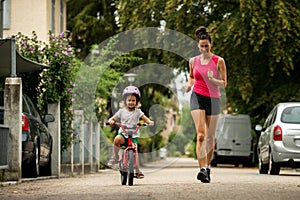 Beautiful and happy young mother teaching her cute daughter to ride a bicycle