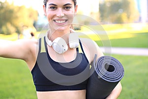 Beautiful happy young sports woman holding fitness rug in urban park