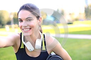 Beautiful happy young sports woman holding fitness rug in urban park