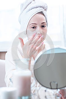 Beautiful happy young woman applying cream on face moisturizing the skin. Concept of hygiene and care for the skin