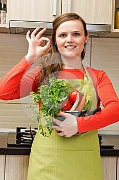 Beautiful happy young woman with apron holdin a pot and making o