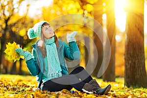 Beautiful happy young woman in the autumn park. Joyful woman wearing bright teal hat and scarf is having fun outdoors in a bright