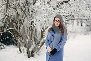 Beautiful happy young woman with black glasses wearing winter coat color Blue Cobalt and black scarf covered with snow