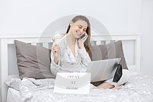 Beautiful happy young woman with a glass of water working on laptop computer in the bedroom. Stay at home. Freelancer. Writing,