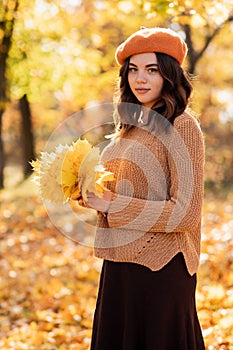 Beautiful happy young woman in park in fall holding leaves. Teenage girl standing outdoors in autumn. Vibrant colors