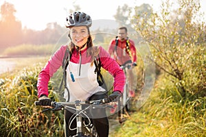 Beautiful happy young woman riding mountain bike over a meadow by the lake or river in the early morning