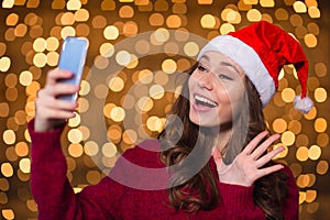 Beautiful happy young woman in santa claus hat using smartphone