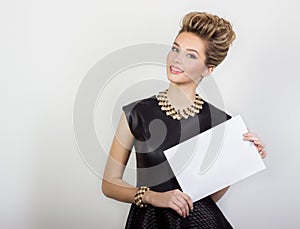 Beautiful happy young woman smiling in a black evening dress with hair and make-up with jewelry a white sign in his hands