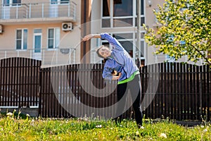 A beautiful happy young woman in sports clothes is doing sports in the yard, performing sideways bends. Concept of outdoor sports