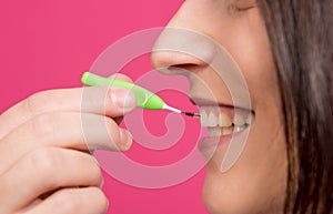 Beautiful happy young woman using interdental brush on the pink background