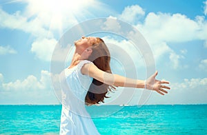 Beautiful happy young woman in white dress on tropical resort island. Vacation Concept. Beautiful girl on the ocean beach raising