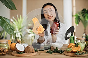 Beautiful healthy asian woman holding pumpkin and bottle with body milk or cream