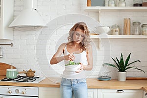 Beautiful healthy casual woman preparing vegetable salad in her kitchen. Healthy lifestyle and healthy diet concept