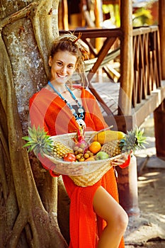 Beautiful healthy young woman is holding basket of tropical frui