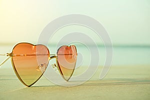 Beautiful heart shaped fashion glasses placed on the beach floor and background sea blur