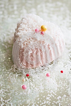 A beautiful heart-shaped pink dessert decorated with coconut flakes and colorful candies, isolated on a mirror background.