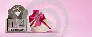 Beautiful heart shaped Valentines Day gift box with ribbon and wooden perpetual calendar on the pink.