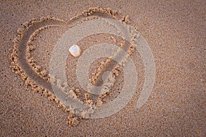 Beautiful heart symbol in beach sand with sea shell in middle. Focus set on seashell