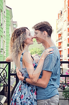 Beautiful heterosexual couple hugging on the balcony. Multicolored urban houses on the background.