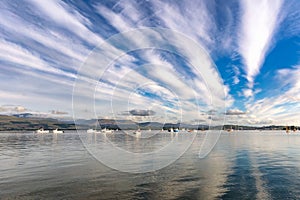Beautiful high level clouds in a blue sky reflecting in a bay with boats. Beaumaris North Wales