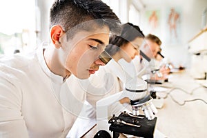Beautiful high school students with microscopes in laboratory.