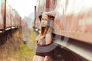 Beautiful hippie girl with red hair and big lips stands near the old car near the railroad