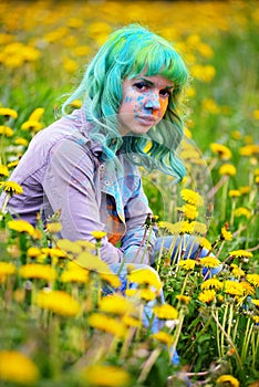 Beautiful hipster alternative young woman with green hair sits in grass with dandelion in park