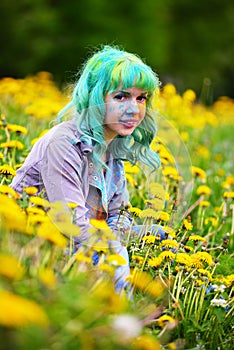 Beautiful hipster alternative young woman with green hair sits in grass with dandelion in park