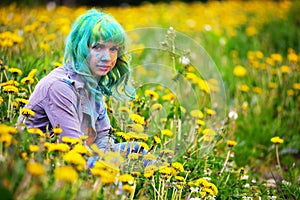 Beautiful hipster alternative young woman with green hair sits in grass with dandelion in park