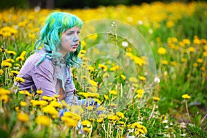 Beautiful hipster alternative young woman with green hair sits in grass with dandelion in park