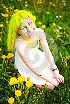 Beautiful hipster alternative young woman with yellow hair sits in grass with dandelion in park