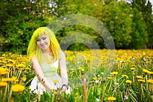 Beautiful hipster alternative young woman with yellow hair sits in grass with dandelion in park