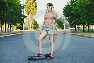 beautiful, hipster blonde with blue hair in tattoo stands with a longboard