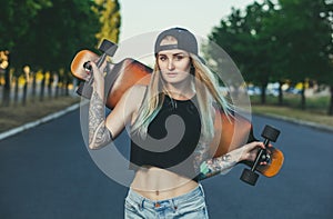 A beautiful, hipster blonde with blue hair in tattoo stands with a longboard