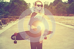 A beautiful, hipster blonde with blue hair in tattoo stands with a longboard