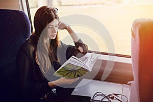 beautiful hipster girl traveling by train and holding book. stylish happy woman reading book at window light in train. travel and