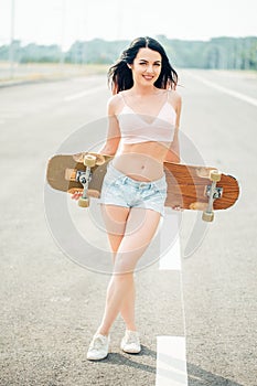 Beautiful, hipster stands with a longboard it is turned back on the street.