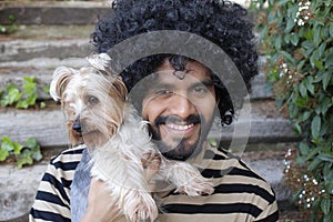 Beautiful Hispanic man with curly hairstyle holding Yorkshire terrier dog