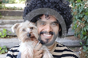 Beautiful Hispanic man with curly hairstyle holding Yorkshire terrier dog