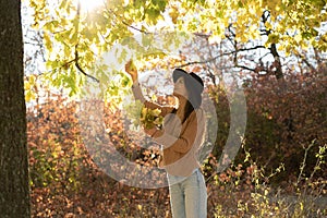 Beautiful hispanic woman with autumn yellow leaves in the city park. Joyful lady during fall.