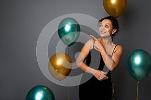 Beautiful Hispanic woman in black velvet evening dress, smiles looking to the side pointing with index finger on copy space on